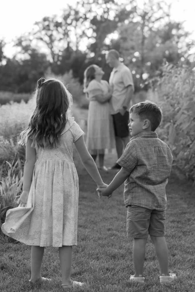 Kids holding hands and looking at Mom and Dad with MelMarie Photography during a family photography session in West Bend Wisconsin