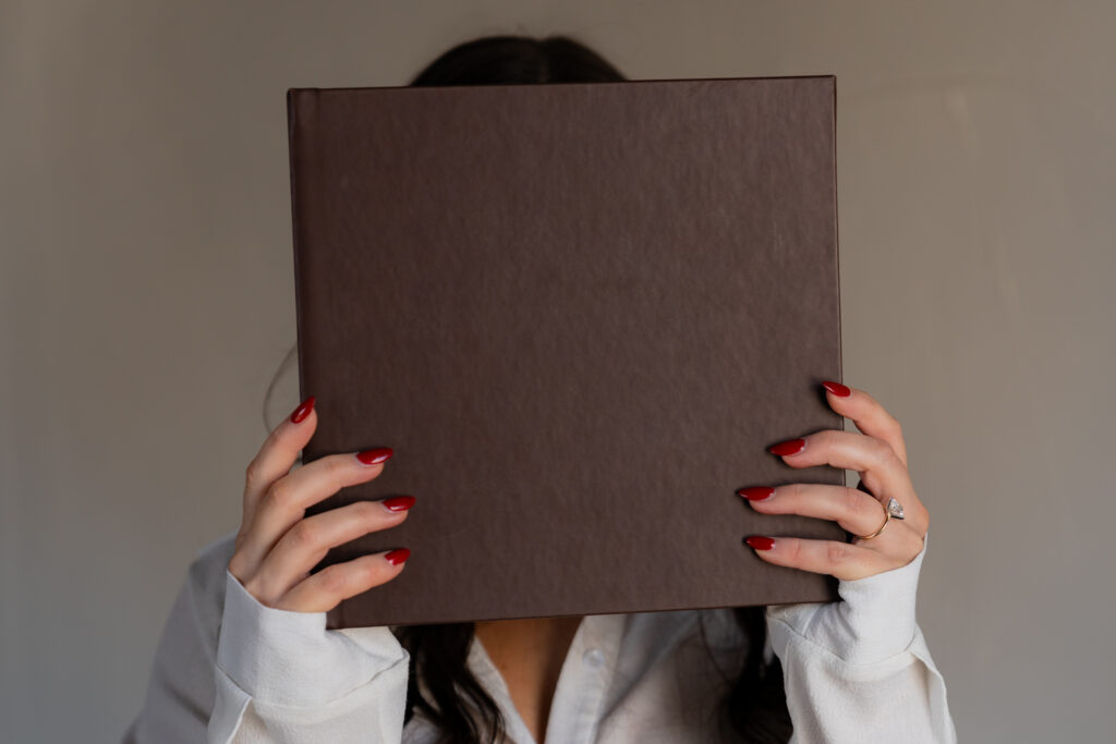 Female holding a brown leather photo album in her hands in front of her face