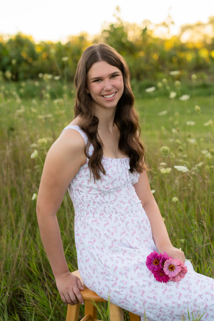 Girl sitting on a wooden stool in a grassy open field and smiling at the camera