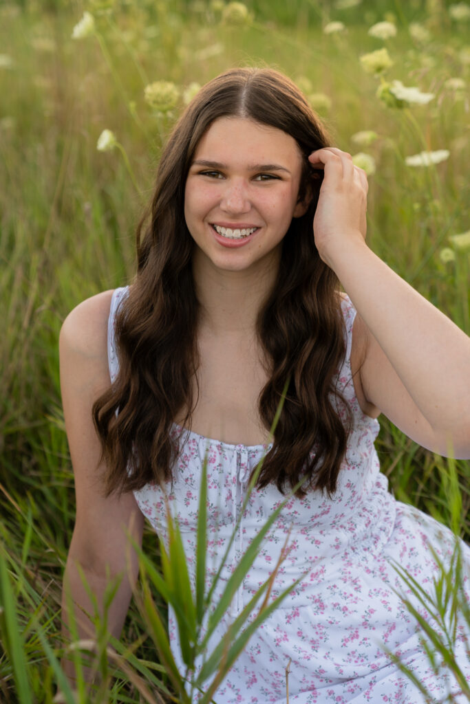 Girl tucking her hair behind her ear while sitting in a field of flowers