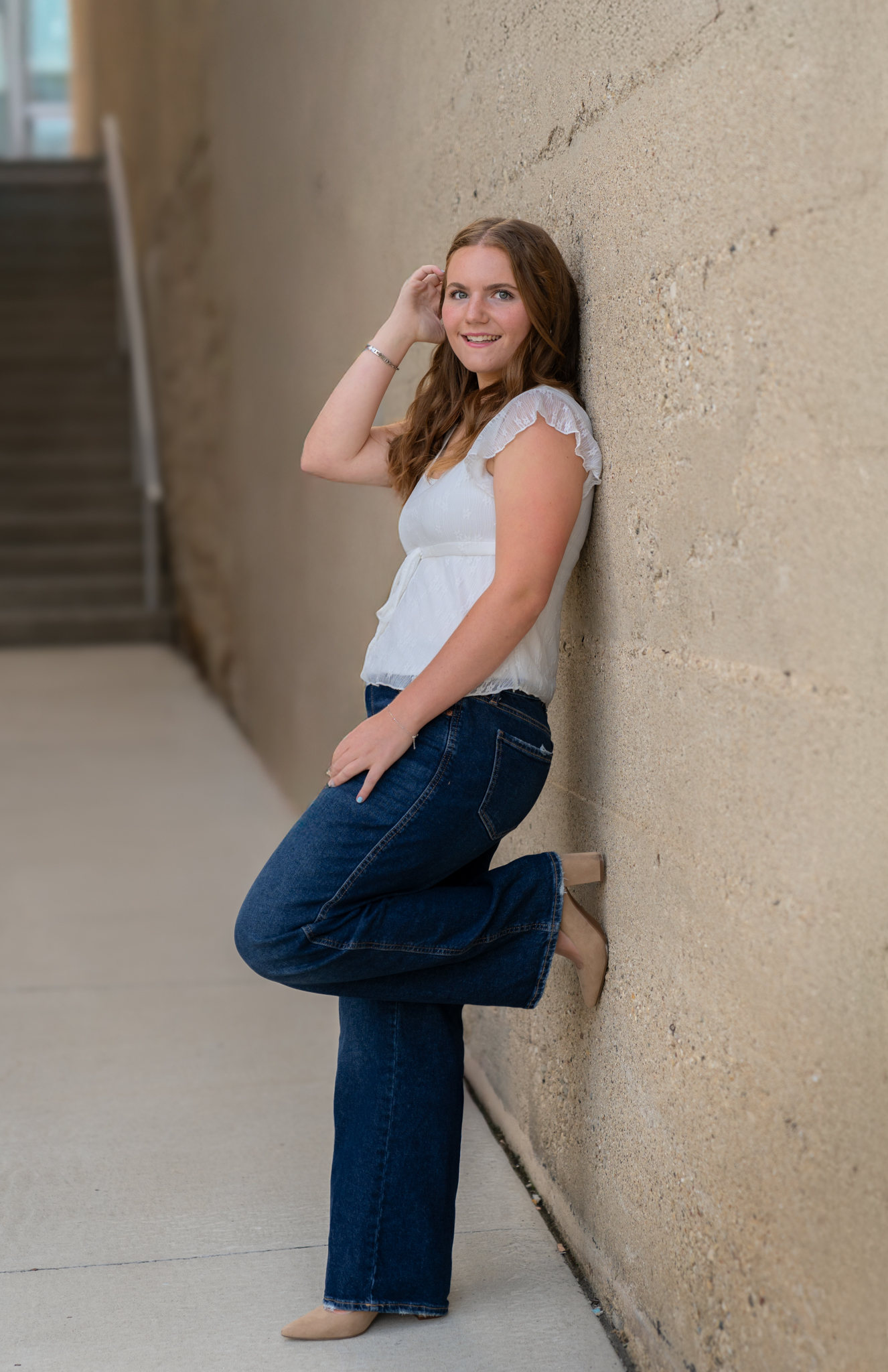 Girl leaning against wall and tucking her hair behind her ear