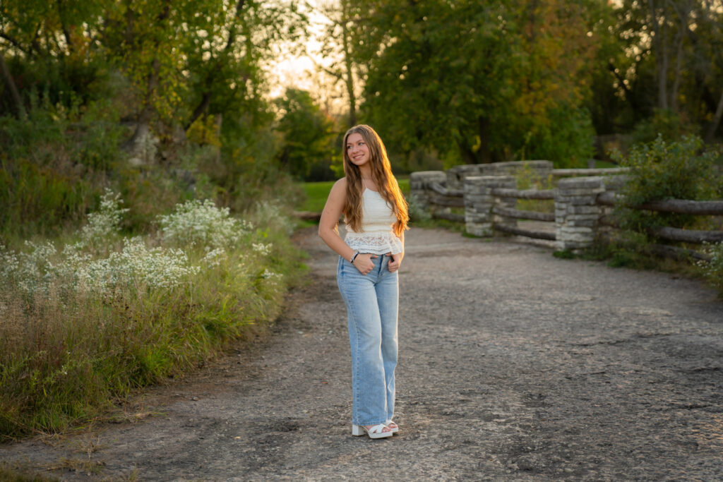 Young senior girl standing in jeans and white tank top beside flowers