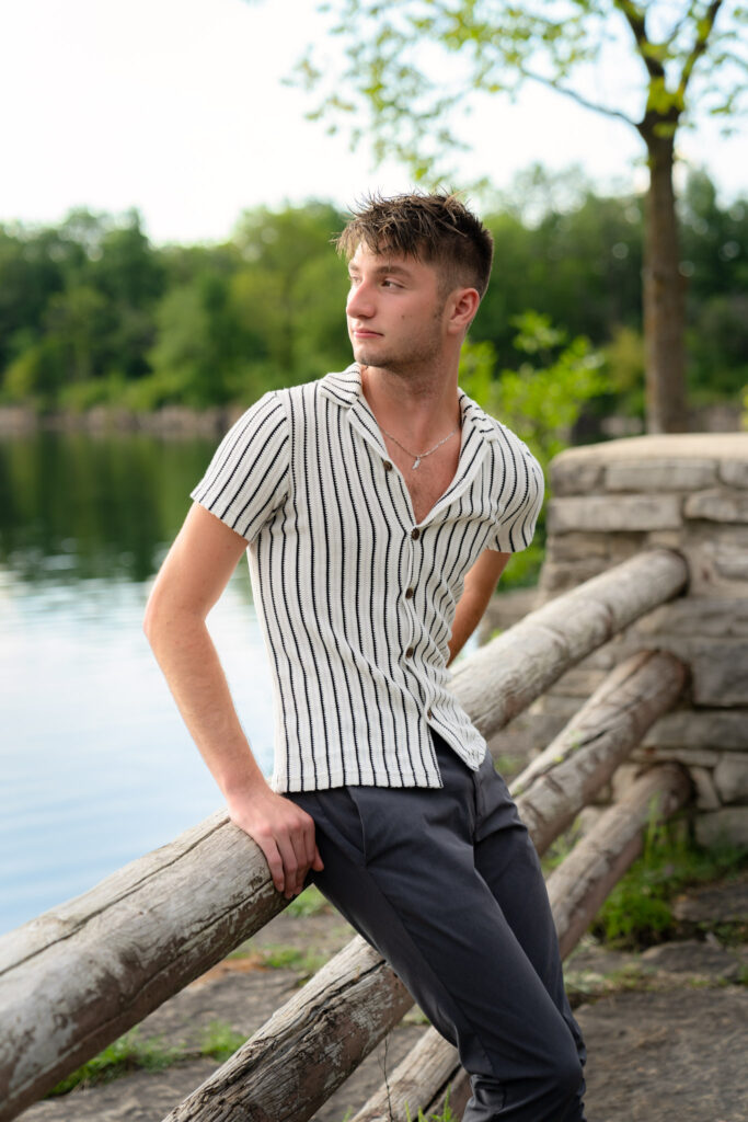 Young boy sitting on wooden railing overlooking a lake
