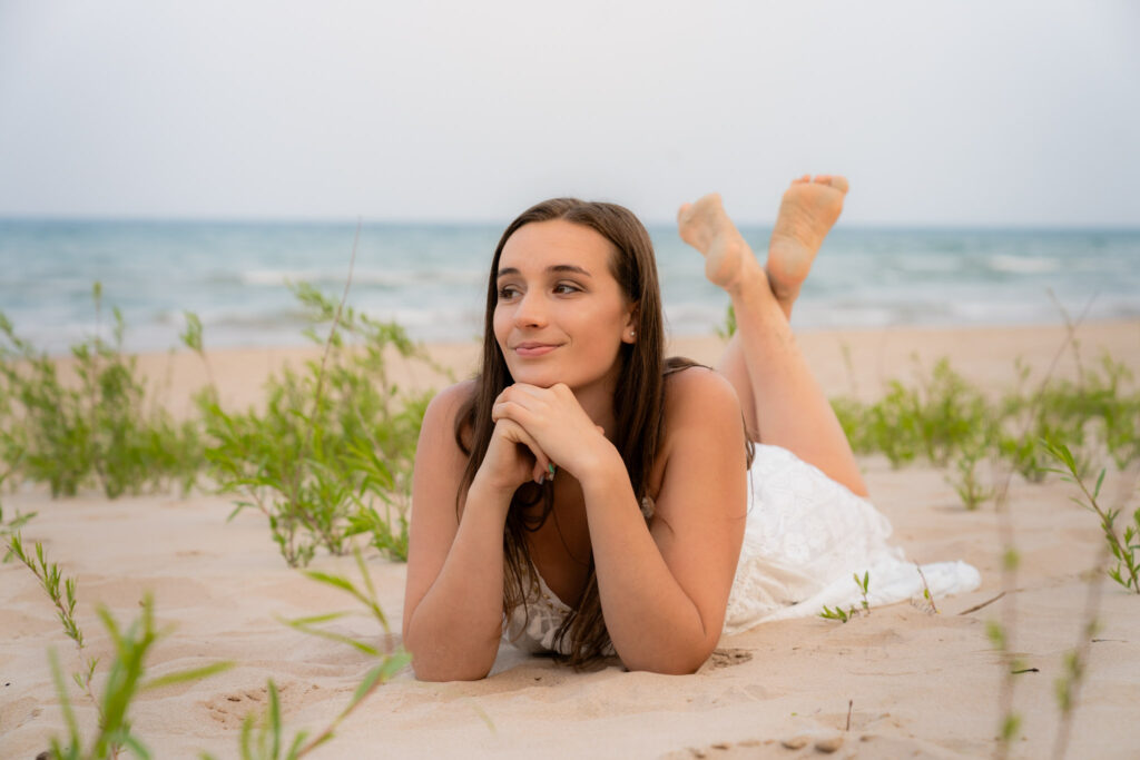 High school girl laying on a beach on her stomach with head in her hands