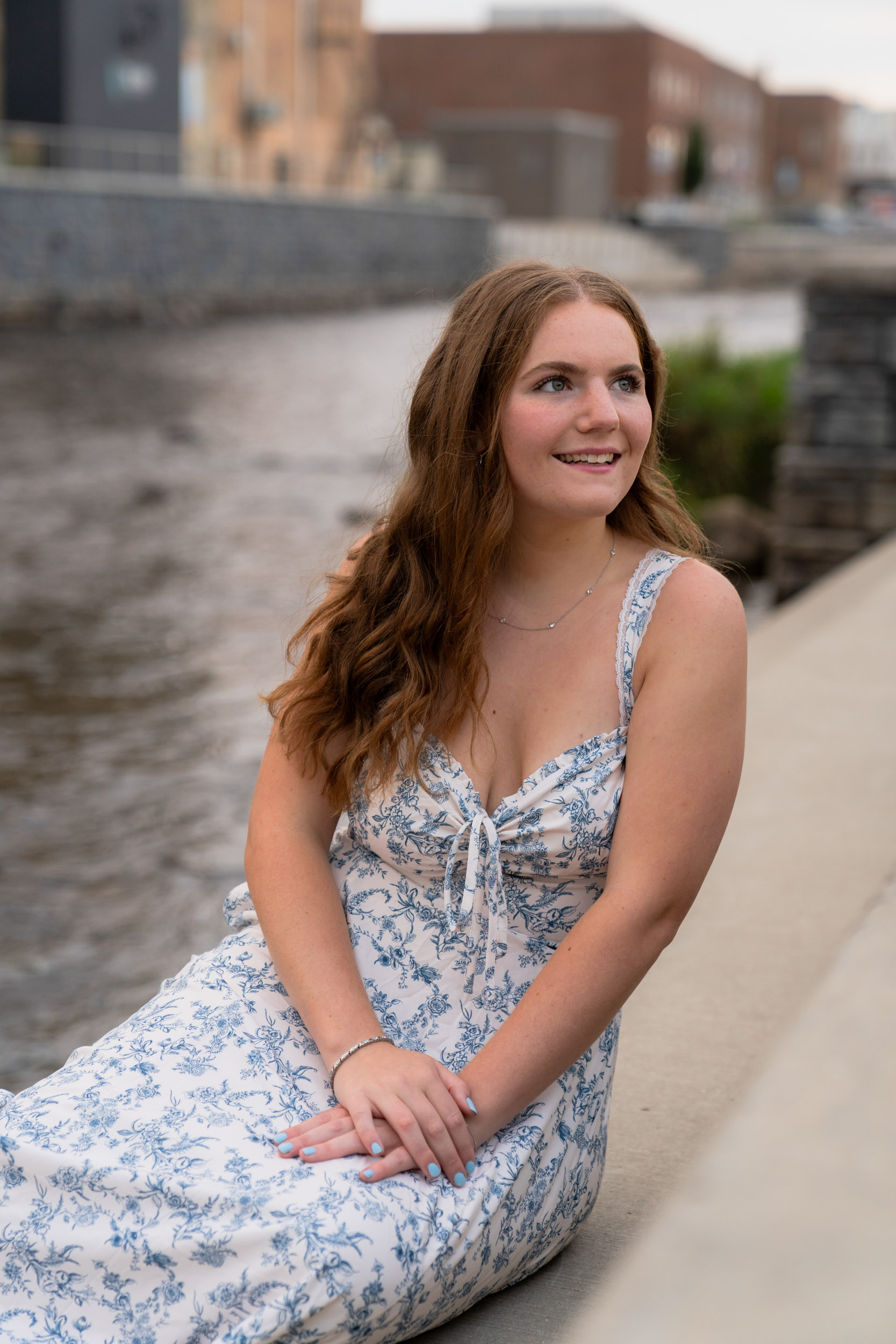Girl in a sun dress sitting alongside a river downtown West Bend Wisconsin