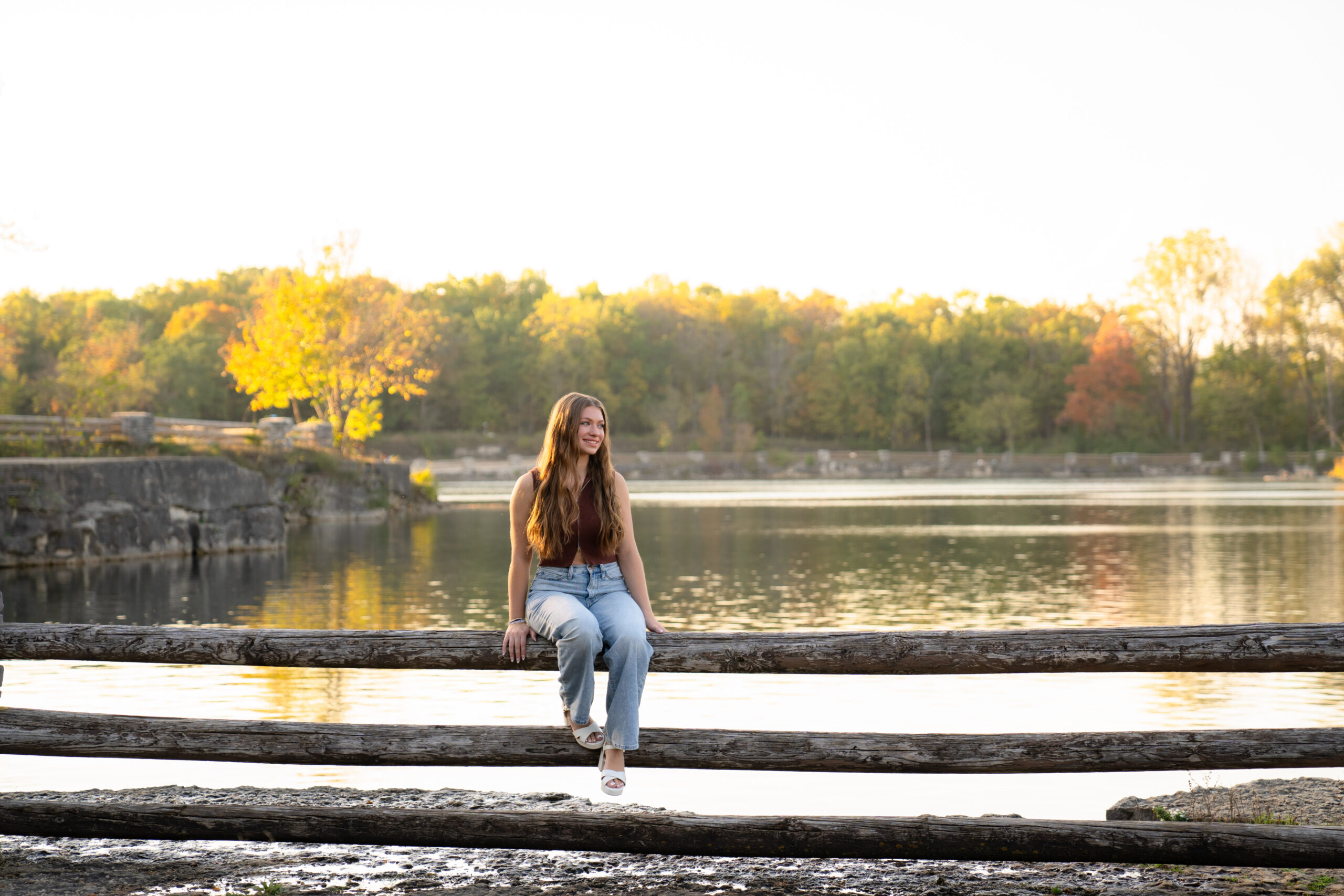 Senior girl sitting on wooden fence at Menomonee Park during a relaxed Menomonee Falls senior session