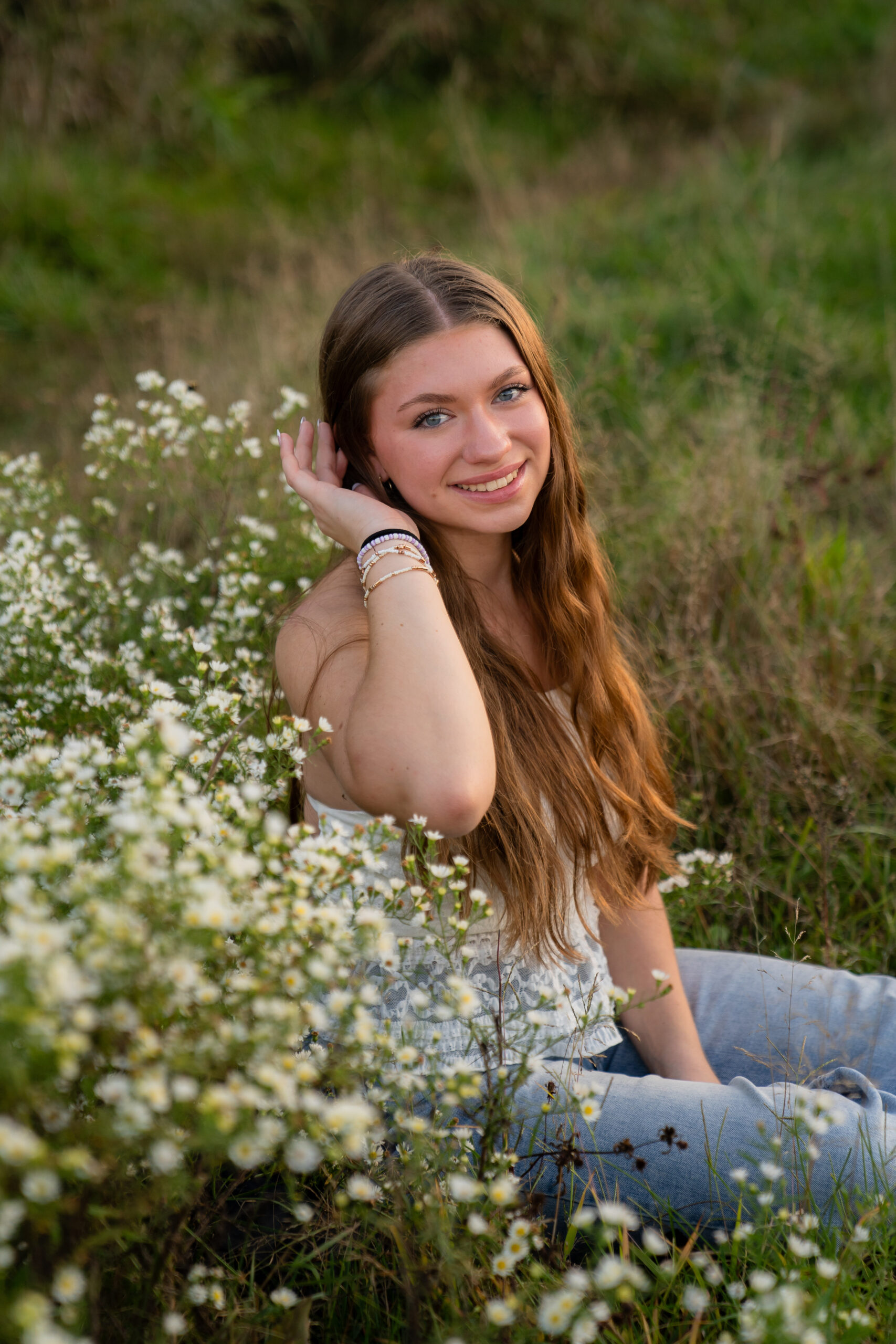 West Bend High school senior posing in white wildflowers while tucking her hair behind her ear and smiling at the camera