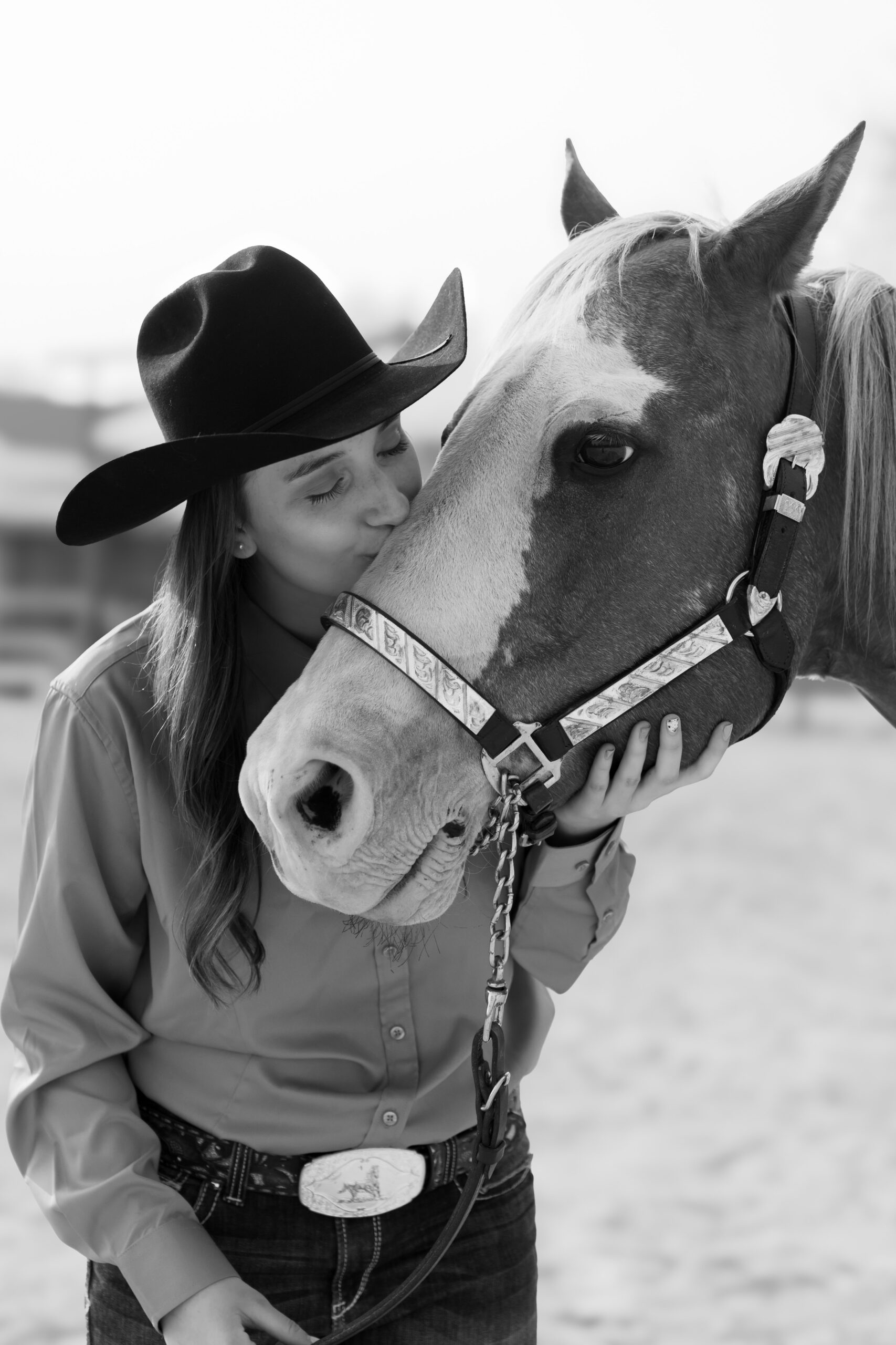 Young lady wearing a cowgirl hat and kissing her horse on the nose