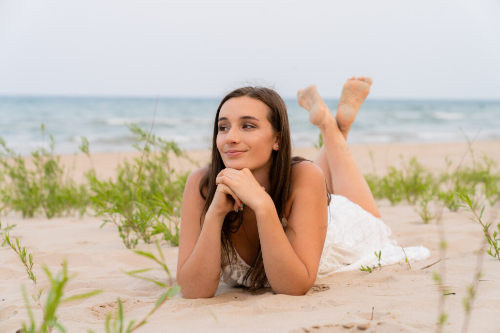 High school senior laying with her head in her hands and smiling during a beach senior photo session in Port Washington, Wisconsin