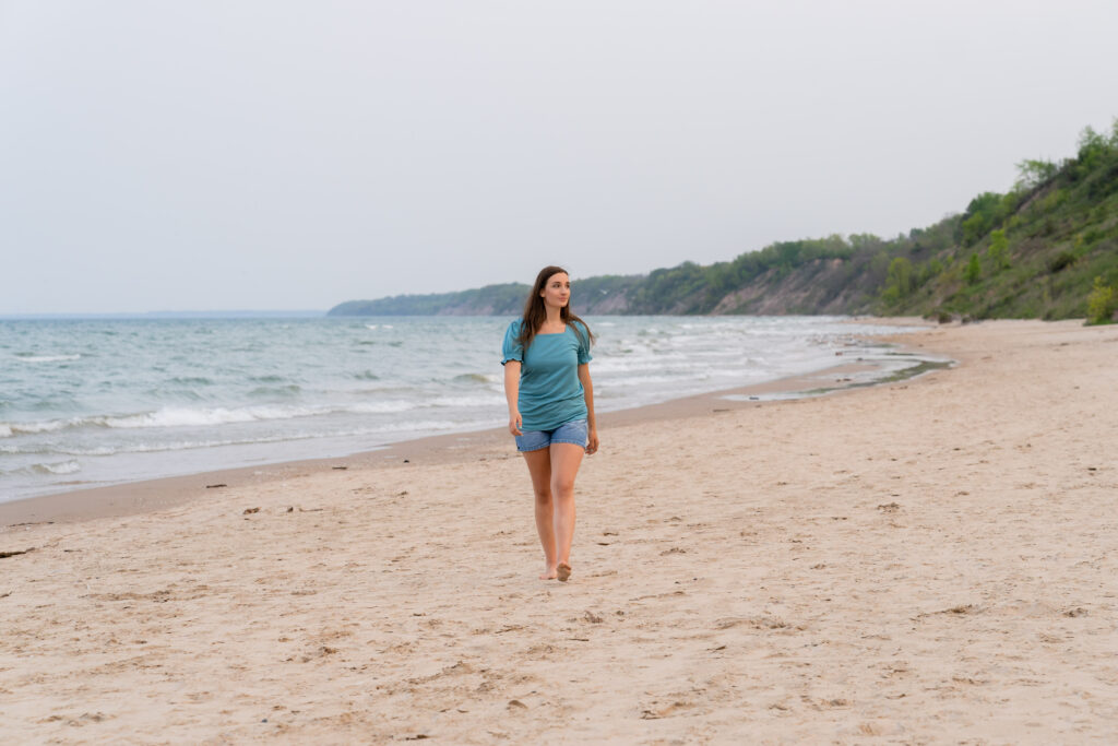 Senior girl walking barefoot in the sand during a relaxed Port Washington senior photography shoot