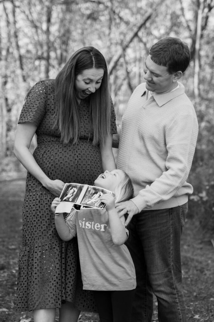 Soon to be big sister holding ultrasound photos while mom and dad smile down at her 