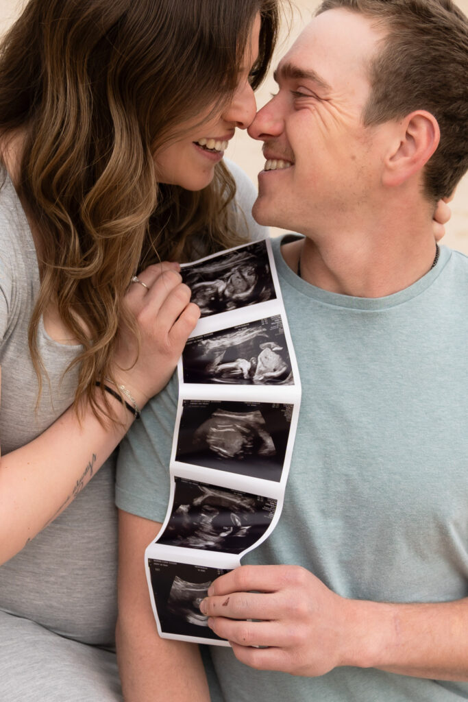 Pregnant mom and partner holding ultrasound photo during a relaxed beach maternity photography session in Cedarburg Wisconsin