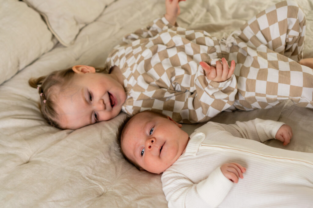 Newborn baby brother and little sister laying on bed next to one another during newborn photoshoot in Waukesha Wisconsin