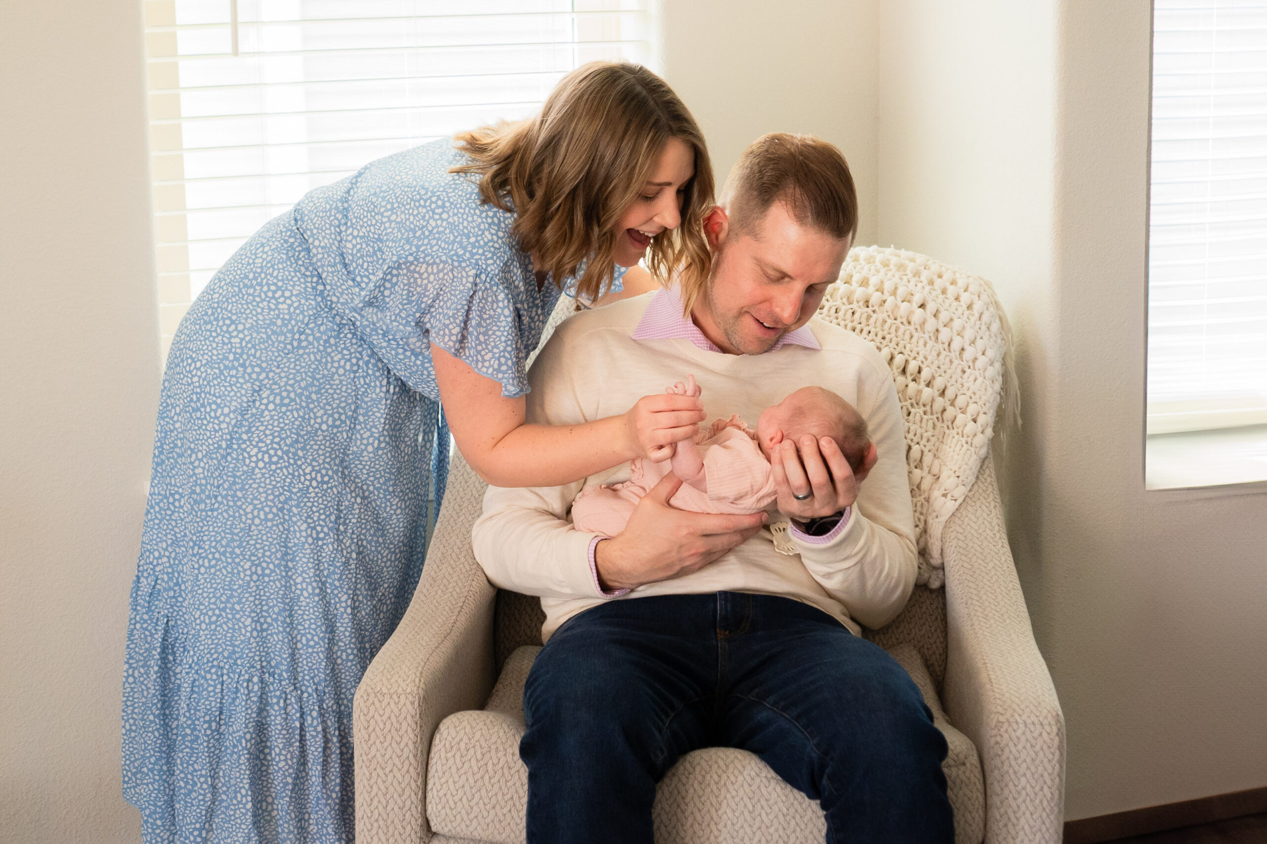 Parents sitting in rocking chair in living room with their swaddled newborn baby
