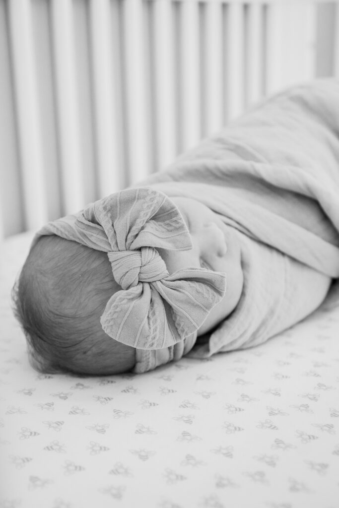 Swaddled baby laying in crib with bow on her head