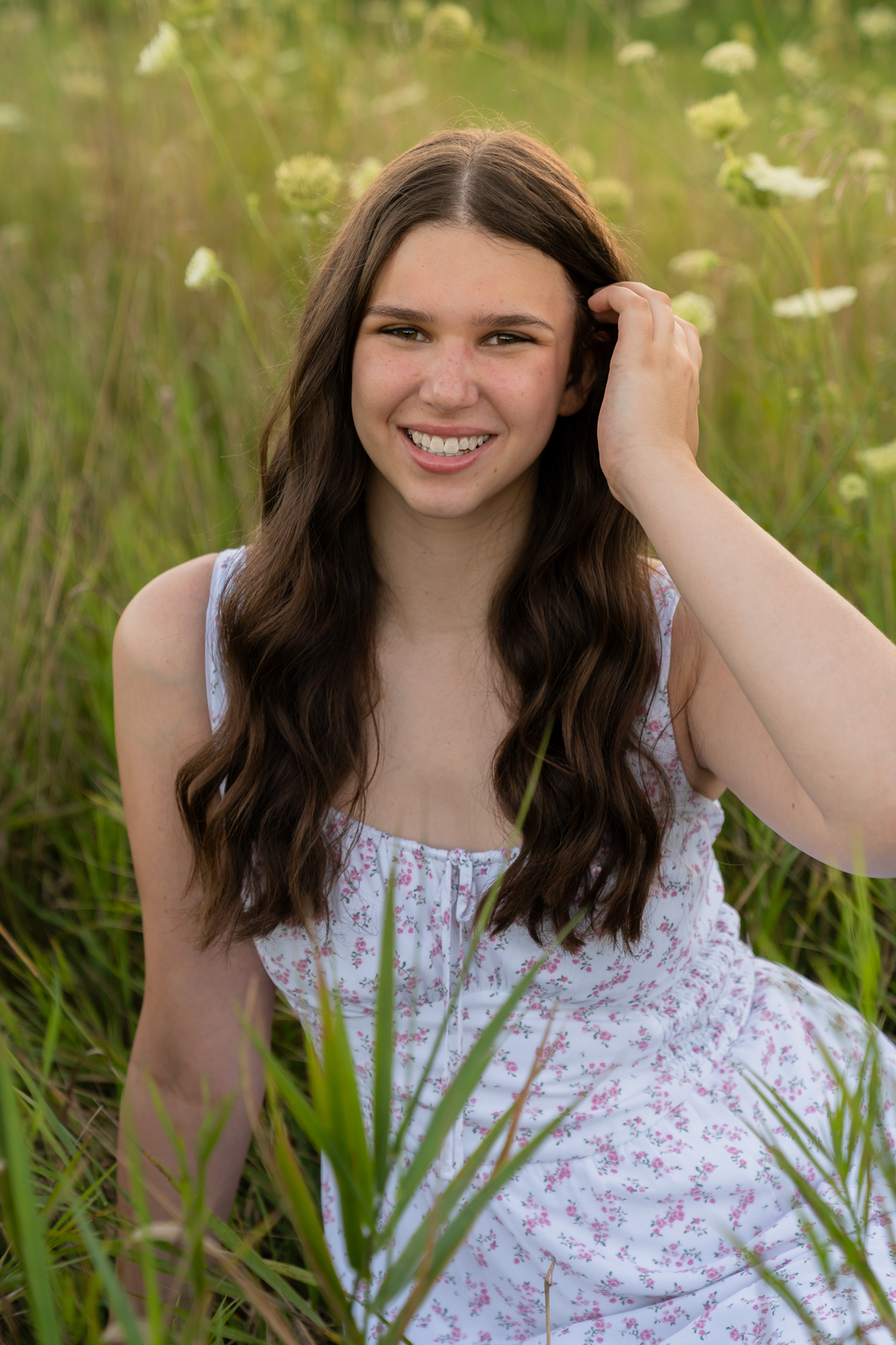 Brunette high school senior sitting in wildflower patch and smiling at the camera