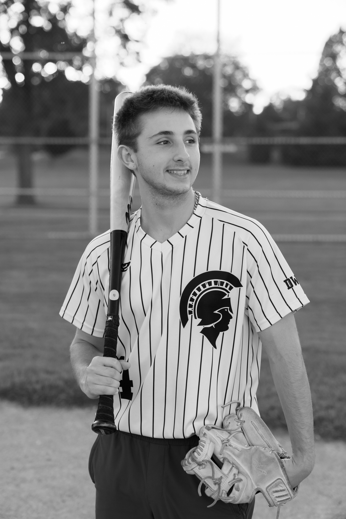Senior boy on the Brookfield East Spartans baseball team holding his bat on his shoulder and smiling off into the distance