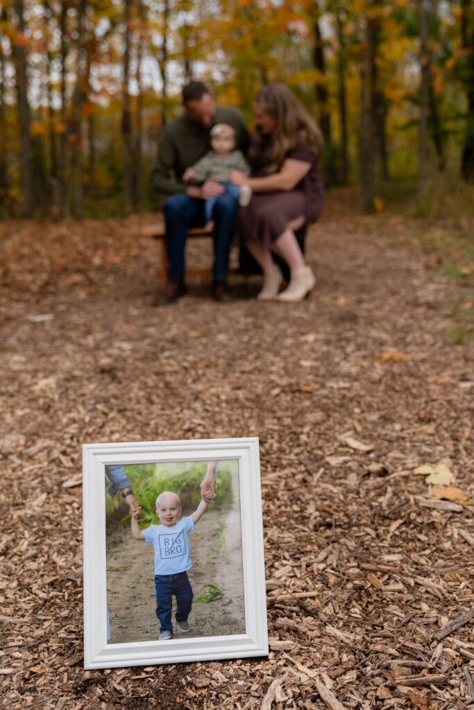 Family portrait with framed photograph in the foreground of photo during outdoor session at Menomonee Park Wisconsin