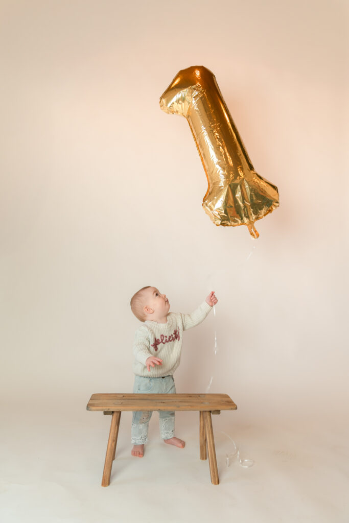 One year old girl holding a big number one balloon during her one year photography session in studio in Cedarburg, Wisconsin