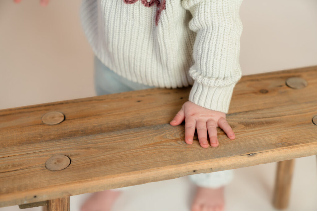 Close up detailed image of Felicity's little hand resting on wooden bench during her one year milestone photography session in studio