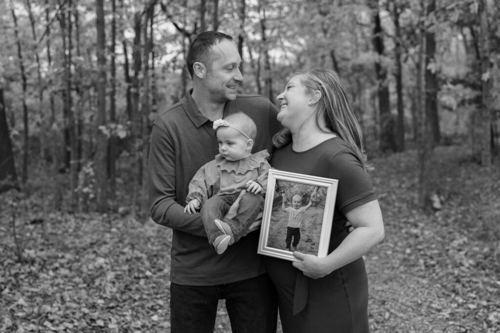 Parents smiling at each other while holding their daughter and framed portrait of their son