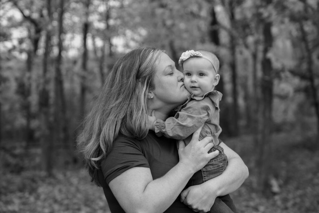 Mother kissing her baby daughter on the cheek during fall mini session