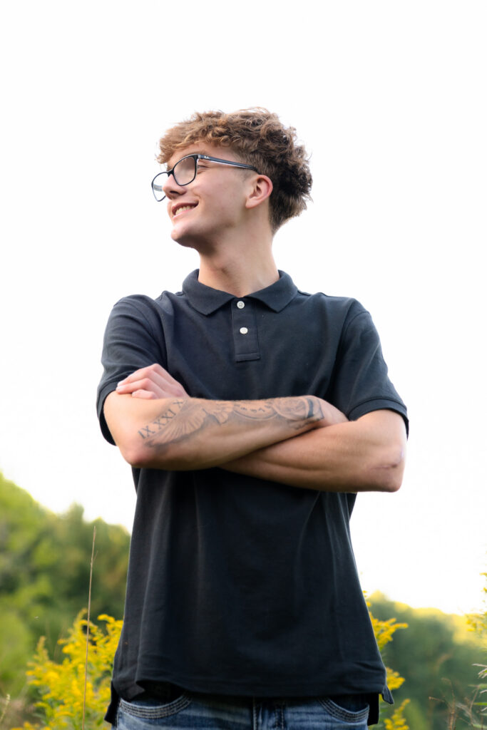 Teenage boy with tatooed arms crossed and smiling candidly during senior photoshoot