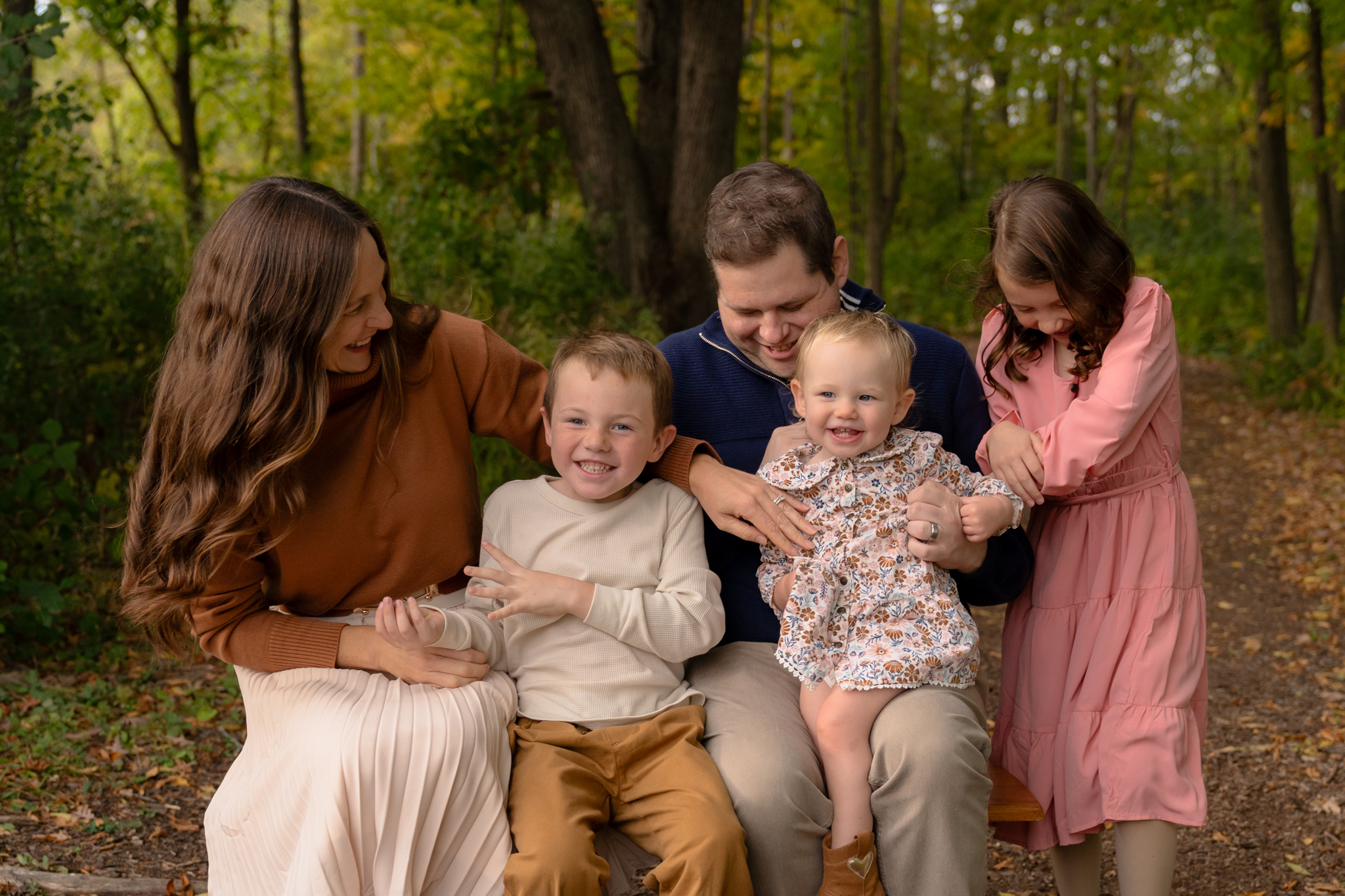 Family candidly laughing with each other while sitting on a bench during their family photography session in Sussex Wisconsin