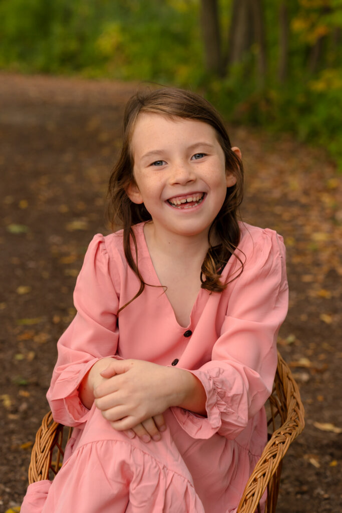 Young girl in pink dress smiling at photographer during family photo session in Menomonee Falls, Wisconsin