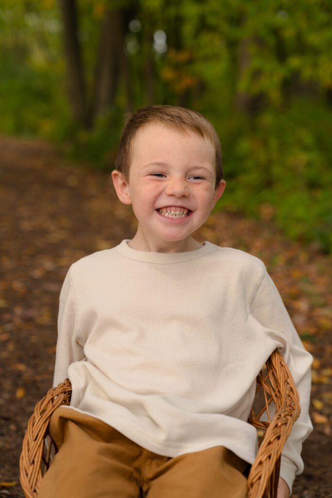Young boy sitting in chair and smiling with his teeth while family photographer takes his photo