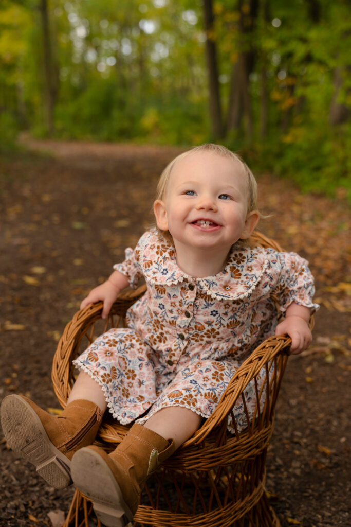 Little girl sitting in a wicker chair and smiling at her parents in Lannon Wisconsin