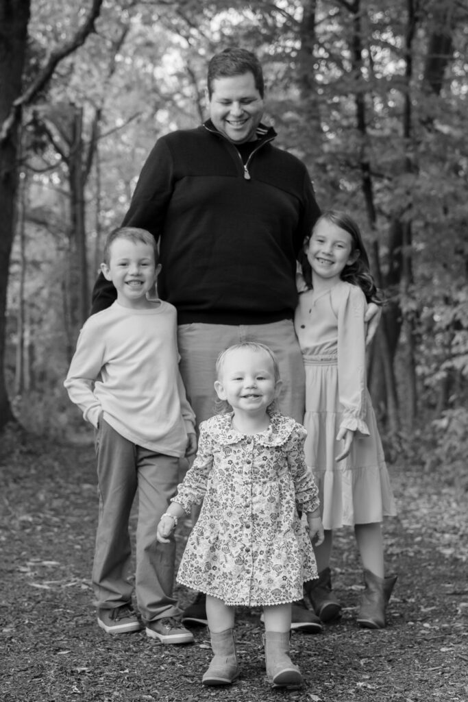 Dad with his arms wrapped around his children and smiling at them in Menomonee Park in Menomonee Falls Wisconsin