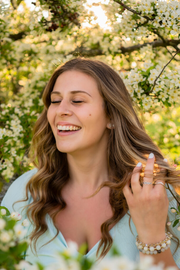 Young woman twirling her hair and candidly laughing with crab apple tree blossoms surrounding her