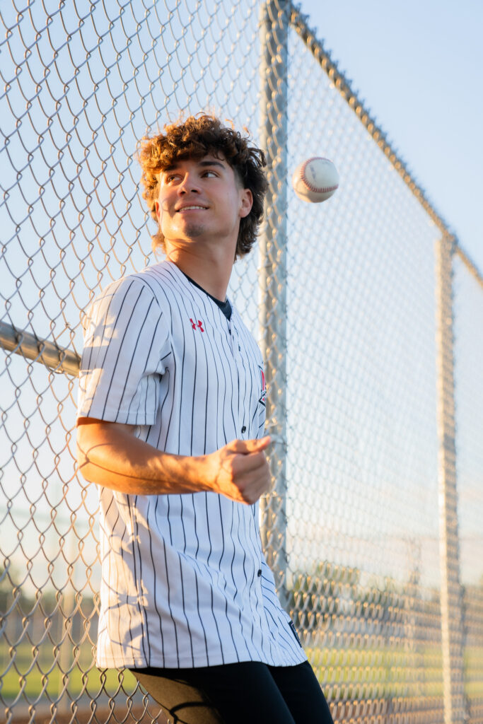 Muskego Wisconsin high school baseball player tossing ball in air and smiling candidly during senior photoshoot