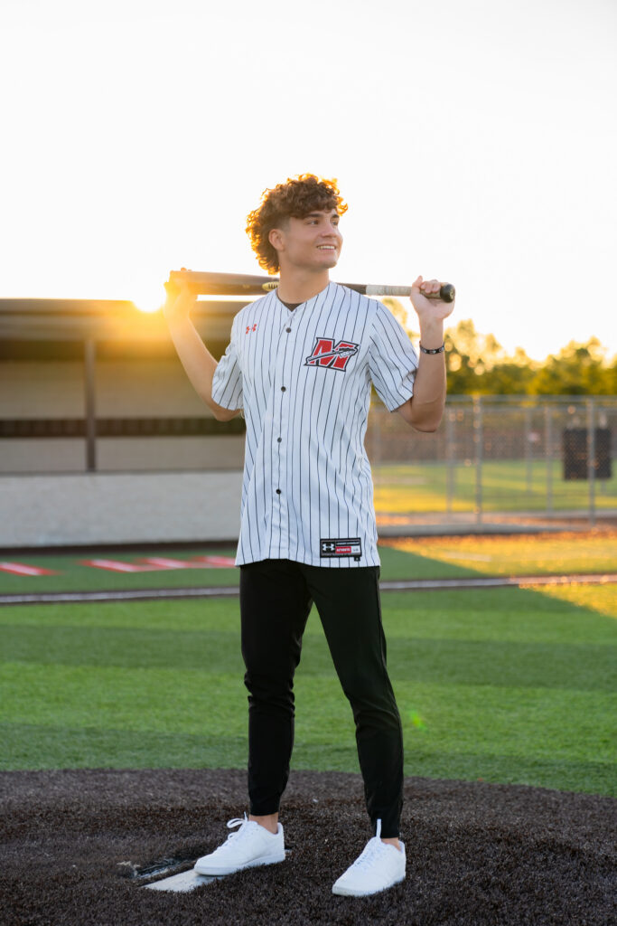 High school baseball player posing with bat during senior photoshoot at Muskego high school