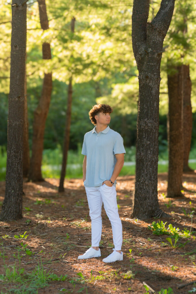 High school boy standing in woods with hands in pocket during senior photoshoot in Muskego Wisconsin