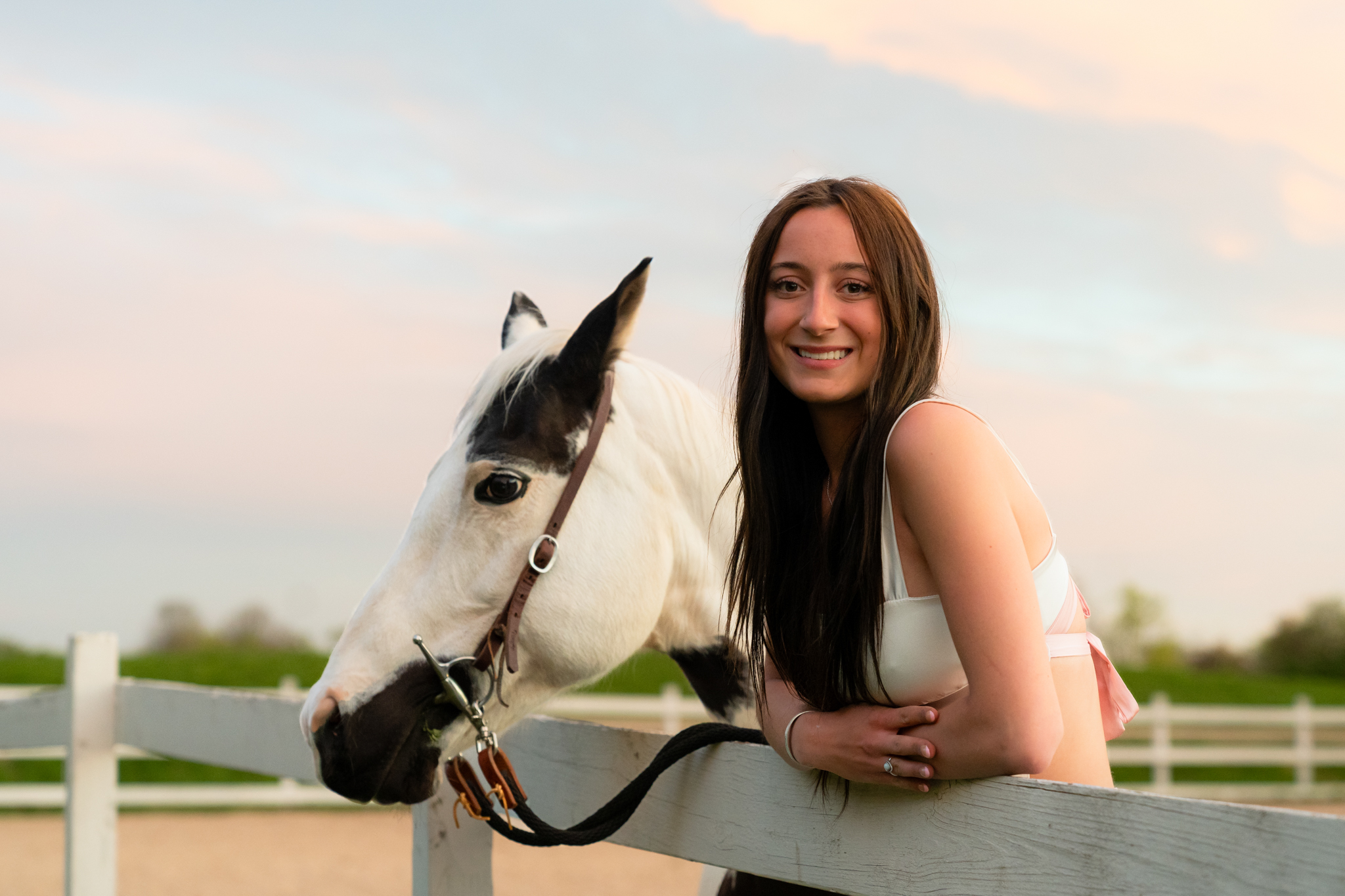Senior girl leaning on fence and smiling at the camera with her horse during photography session in West Bend Wisconsin