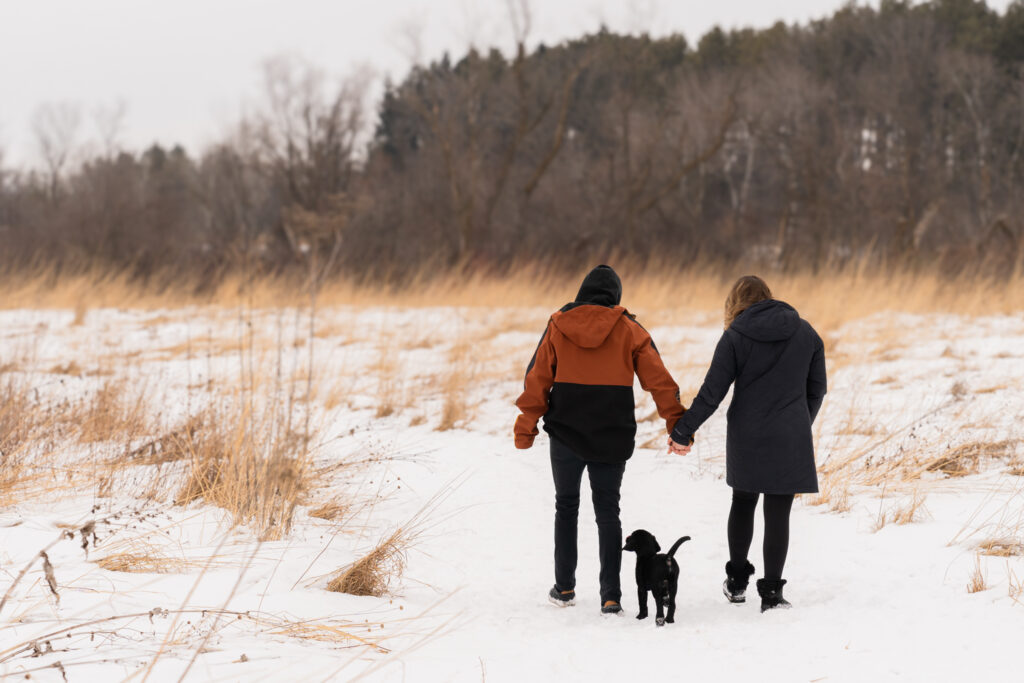 A couple holding hands and walking with their dog through a field during photography session