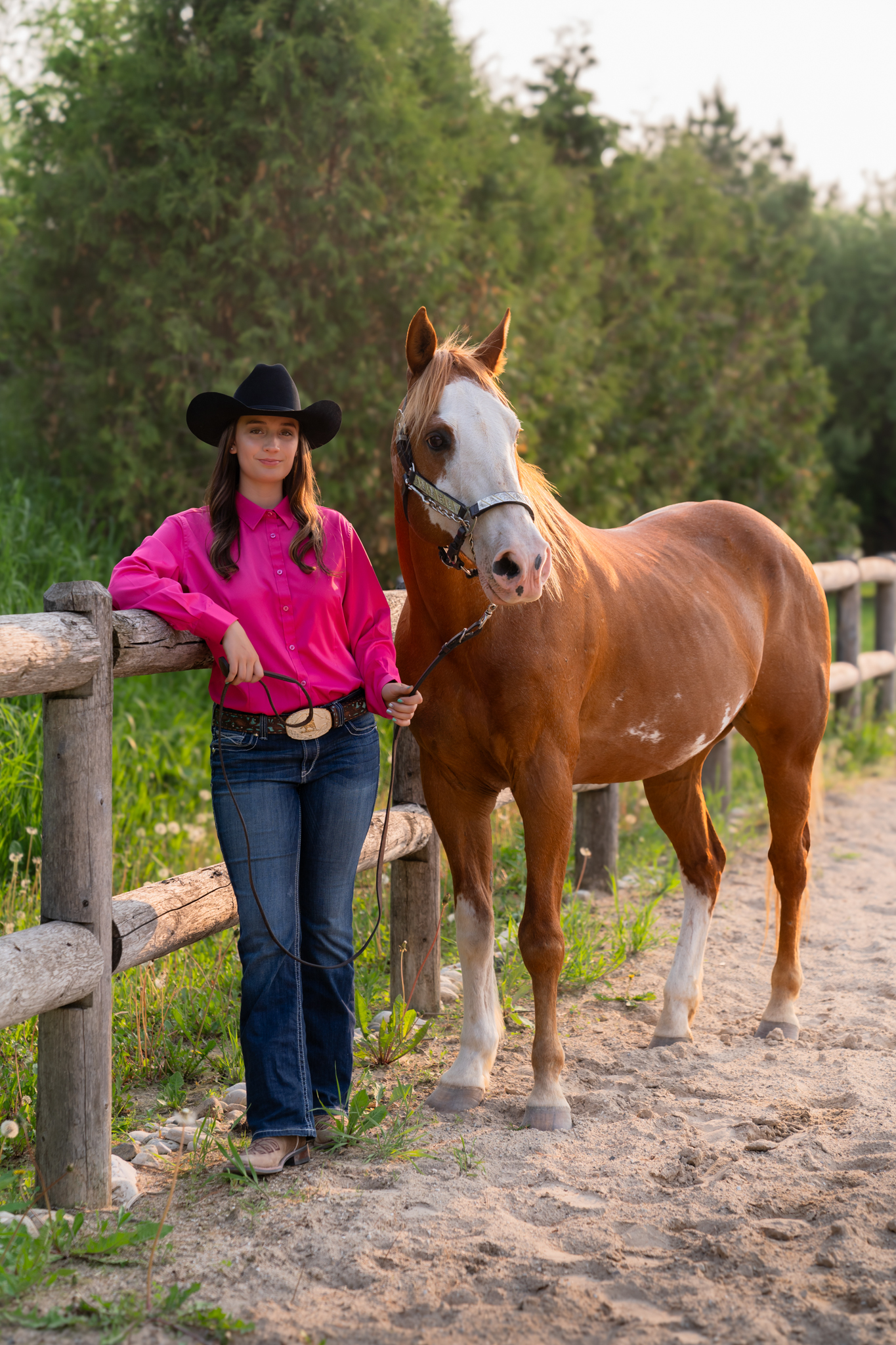 A girl and her horse leaning against a wooden post and smiling during a senior photography session