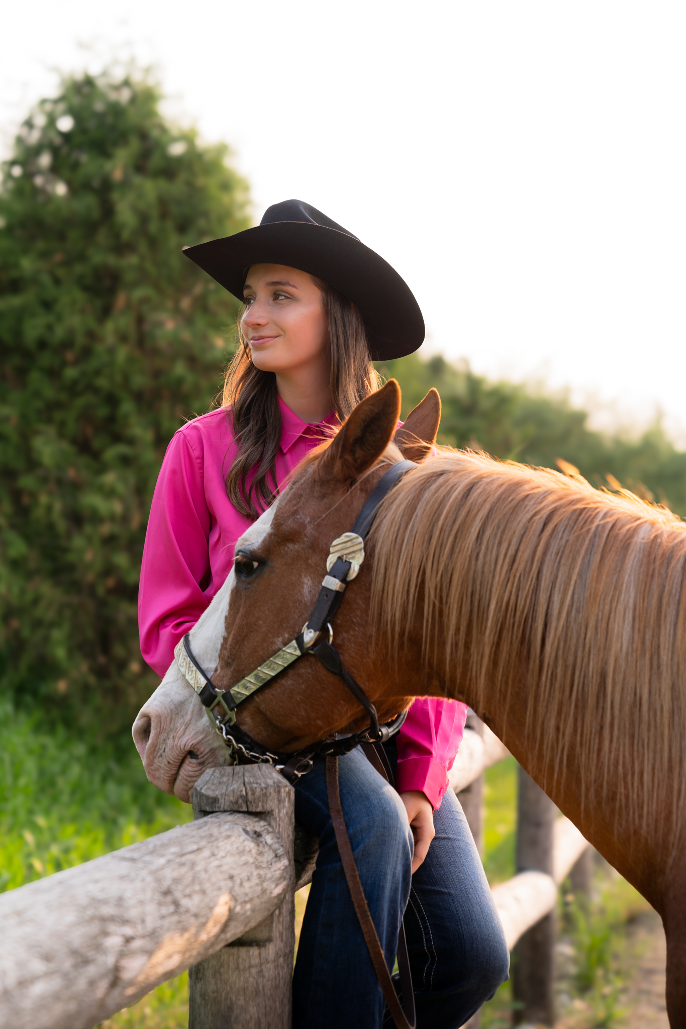 Senior girl wearing a cowgirl hat and sitting on a railing with her horse in Port Washington, Wisconsin