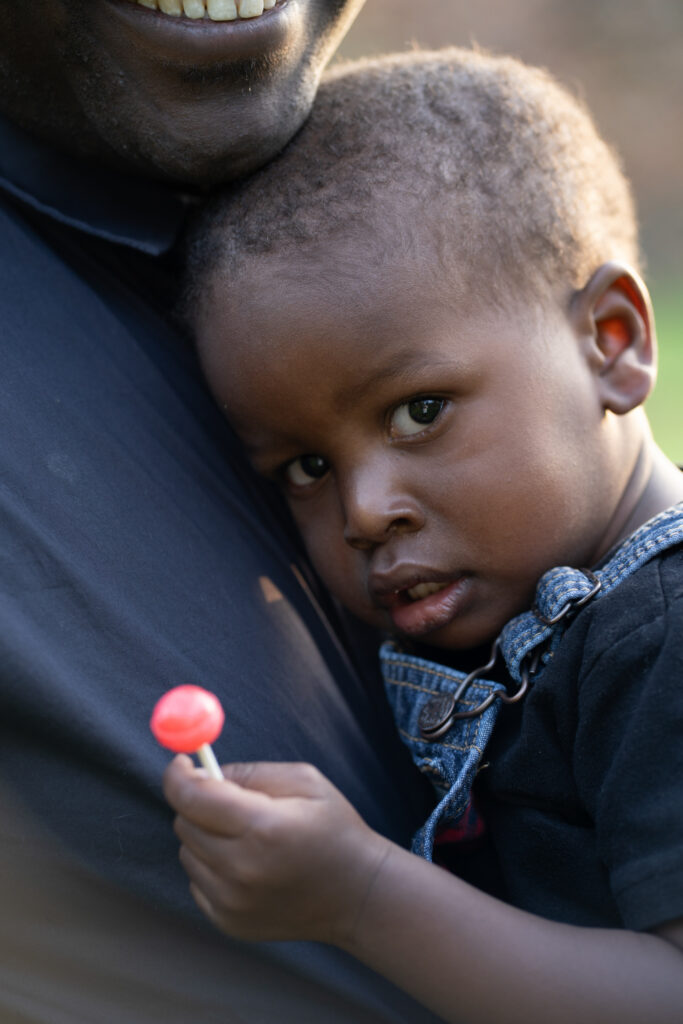 Small boy resting his head on his dads chest with a sucker in his hand