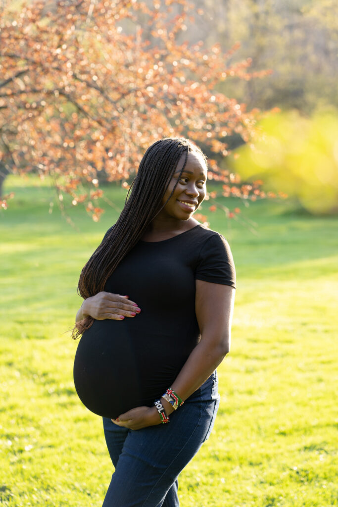 Pregnant mama holding her belly and smiling into the distance during crab apple trees photo session in whitnall park
