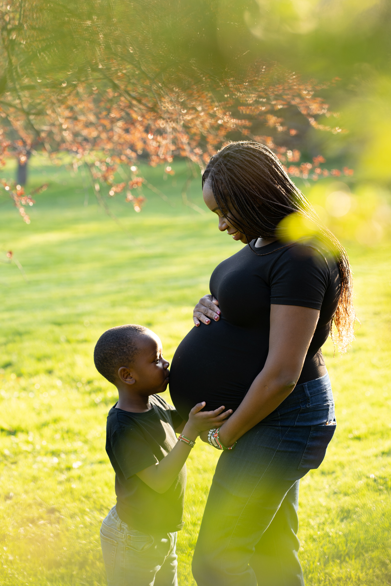 Expecting mother holding her belly while her son kisses it during maternity session in Milwaukee Wisconsin at whitnall park