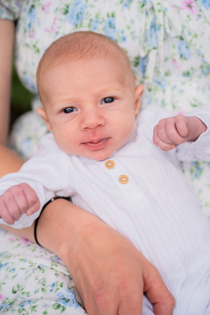 newborn baby smiling at the camera while his mother holds him in her lap