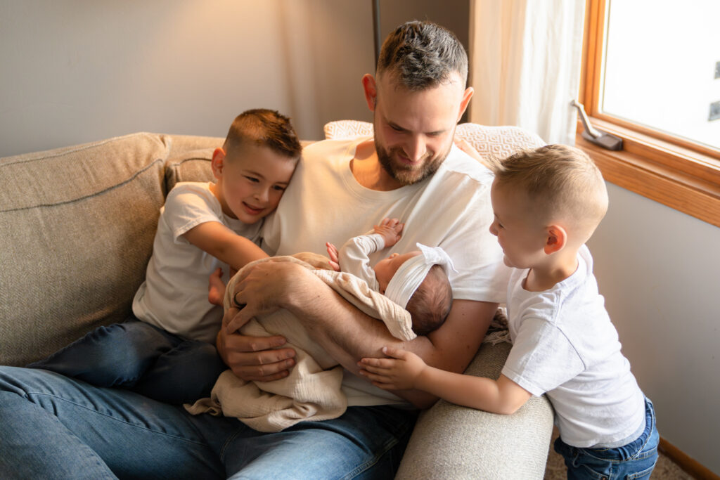 Father holding his newborn baby daughter while his two sons smile at her