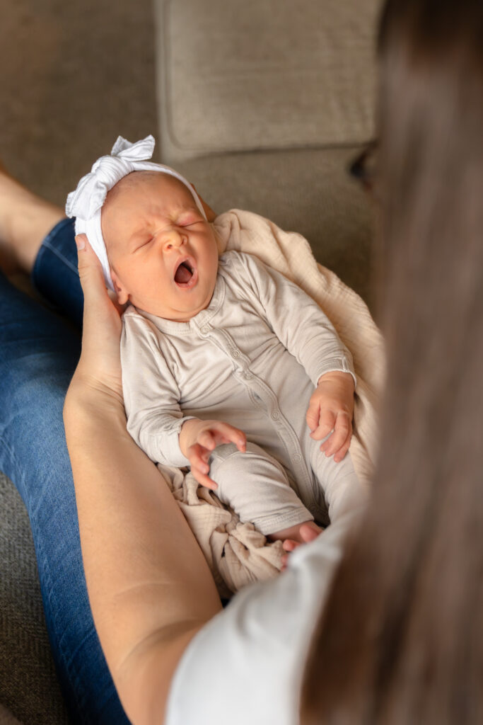 Newborn baby yawning in mothers arms during in-home newborn session in kewaskum wisconsin