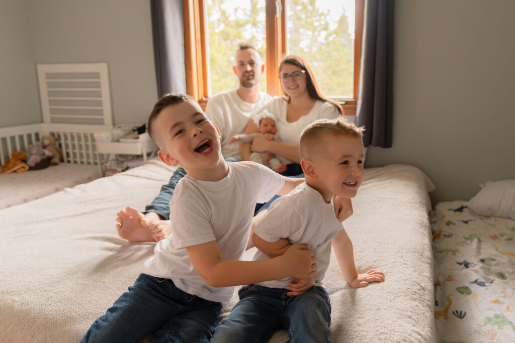 Two young boys goofing around while mom and dad sit in the background with their newborn baby sister